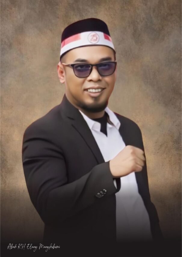 Potret Abah Elang Mangkubumi mengenakan jas hitam dan peci khas Pagar Nusa, mengangkat tangan dengan gesture tegas sebagai simbol seruan moral terhadap kebijakan Pemkab Serang terkait proyek PIK-2.